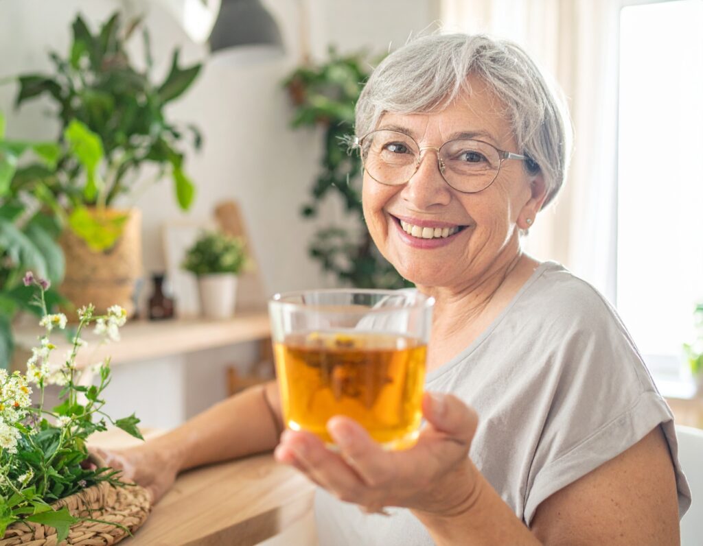 Donna sorridente prepara una tisana erboristica artigianale in cucina con erbe fresche
